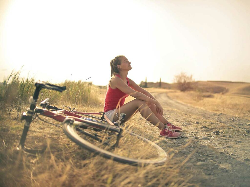 Woman sitting next to her bike on a dirt road enjoying the sunshine