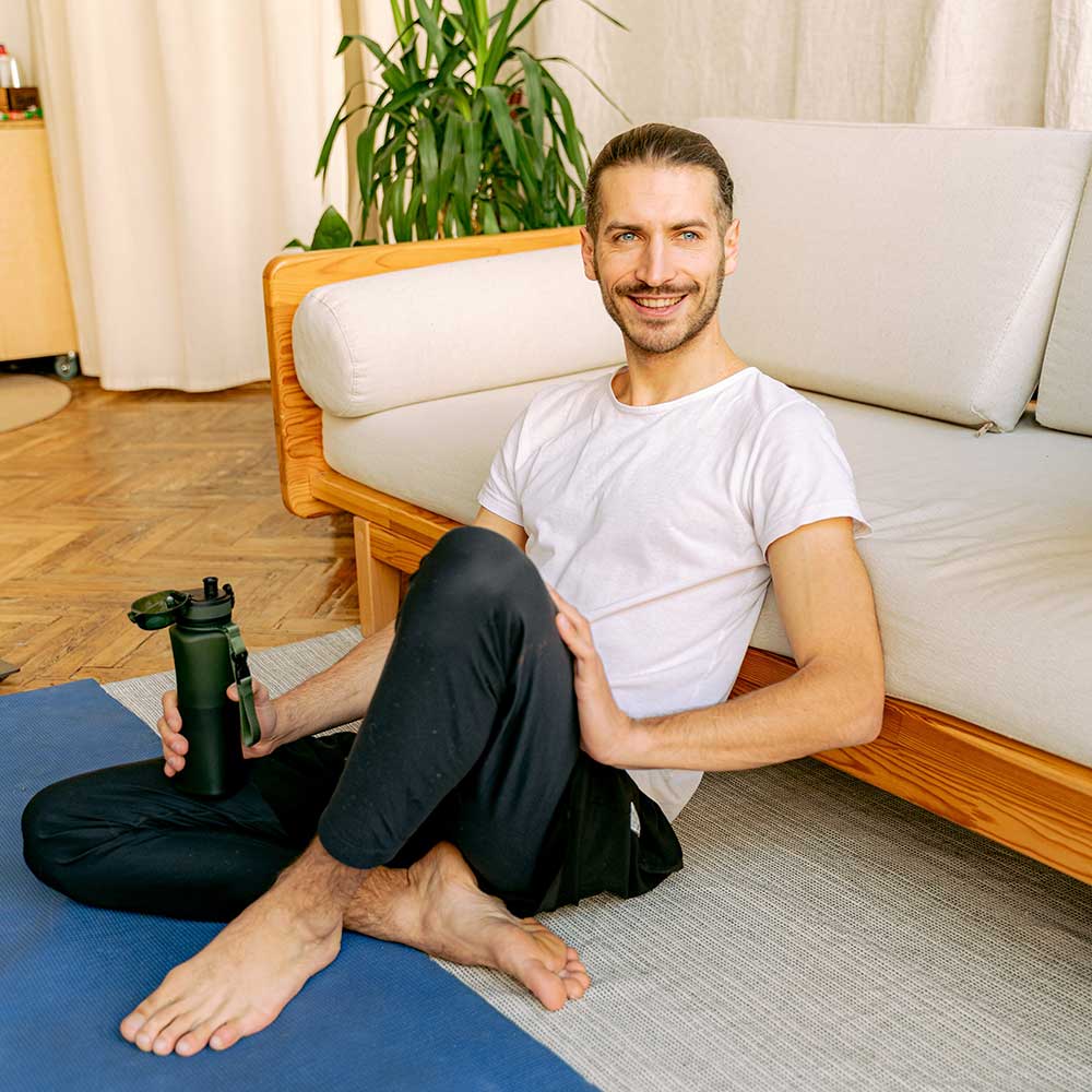 Man sitting on floor drinking water after a workout