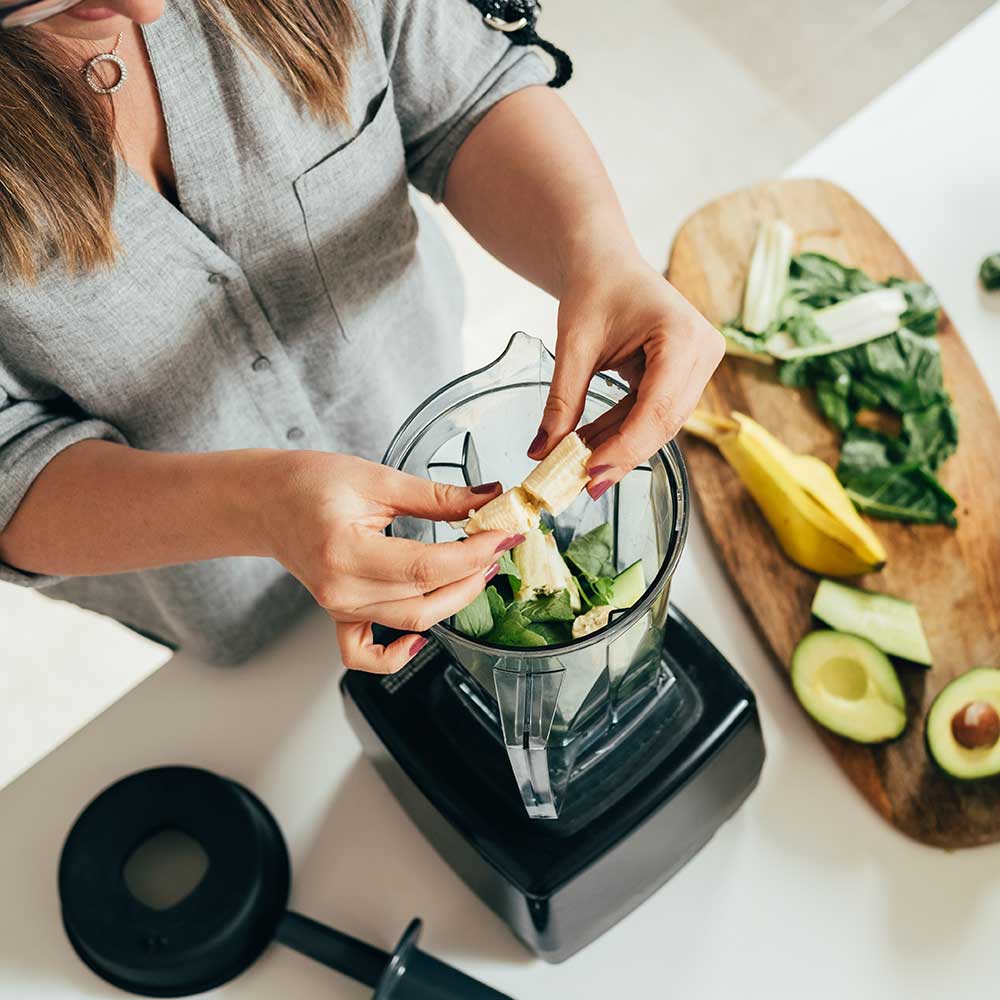 Woman preparing a smoothie in a blender.