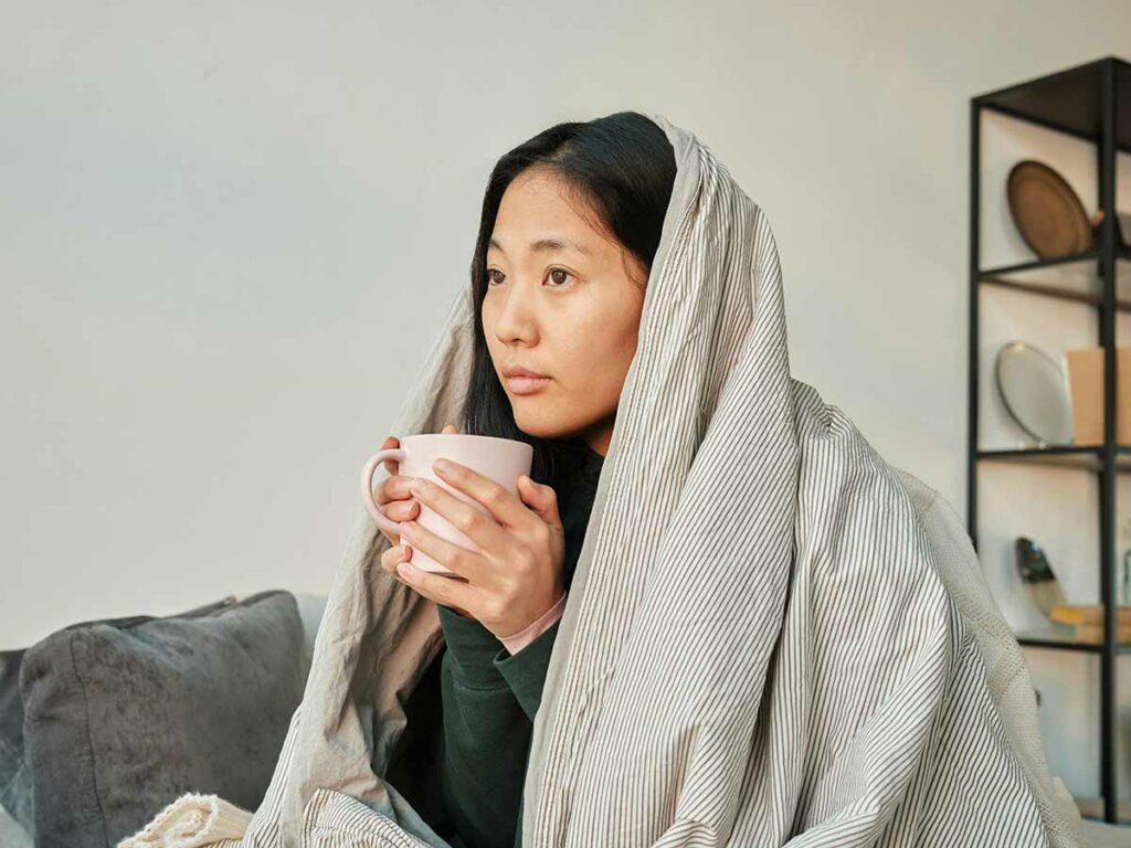 Woman sitting on bed under a blanket drinking a cup of tea